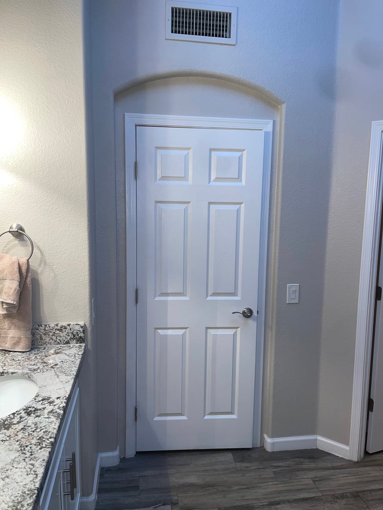 White six-panel interior door in a light blue hallway with arched doorway trim and bathroom sink visible to the left