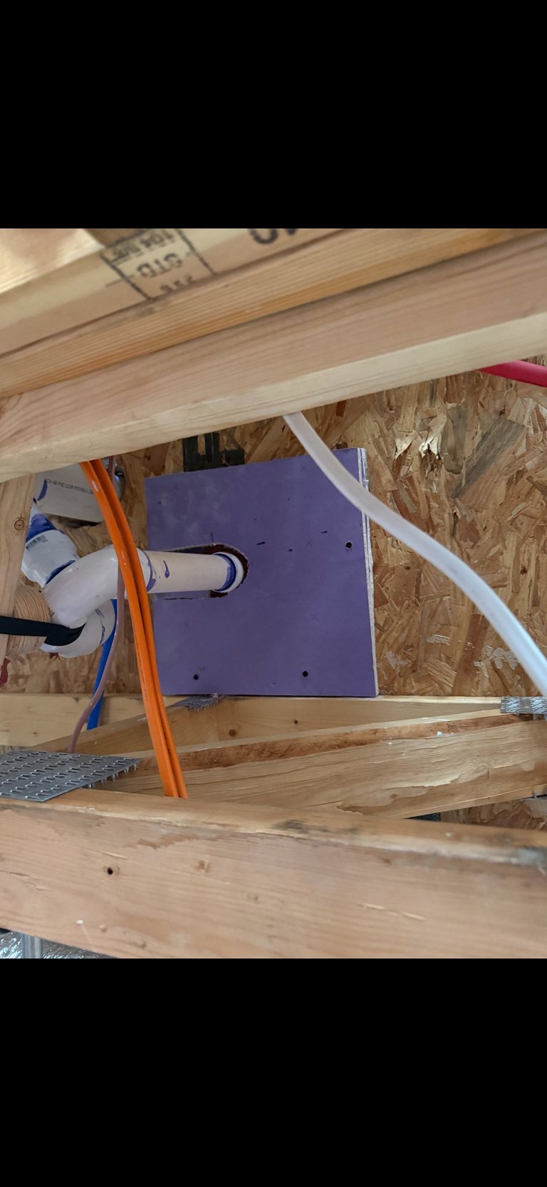 Purple electronic device with cables mounted under wooden shelving and OSB boards in an attic or crawl space