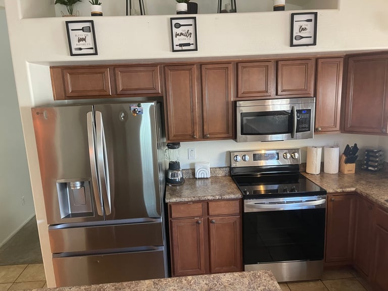 Modern kitchen with wood cabinets, stainless steel appliances, granite countertops, and shelving with decorative items above