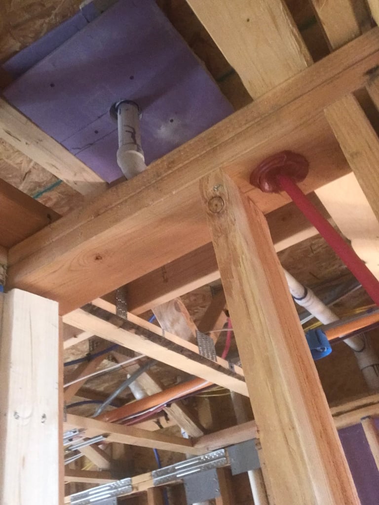 Interior framing construction showing wooden beams and exposed plumbing with purple insulation board on ceiling