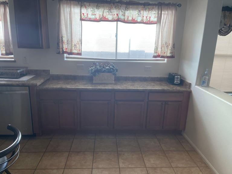 Kitchen counter with dark wood cabinets, granite countertop, and windows with decorative valance above