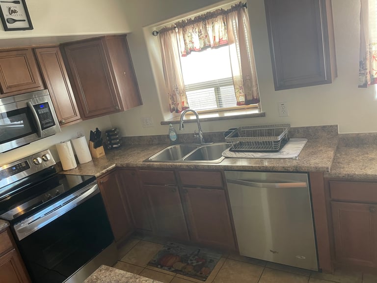 Modern kitchen with brown cabinets, granite countertops, stainless steel appliances, and a window above the sink
