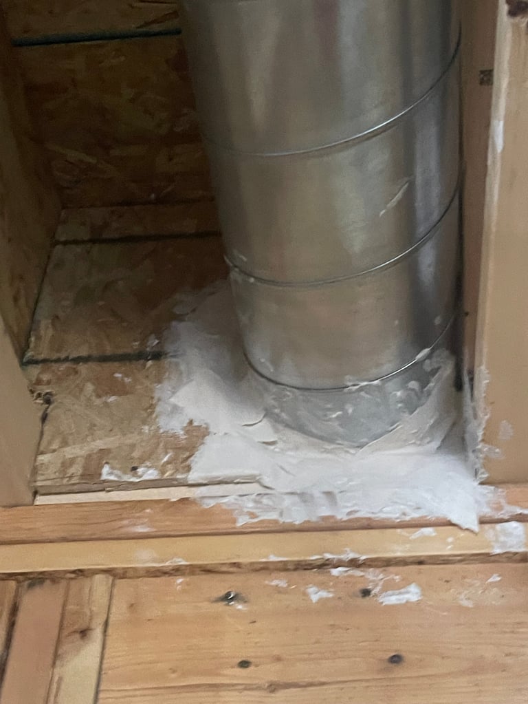 Metal ductwork installed in a basement corner with white drywall compound and wooden subfloor visible