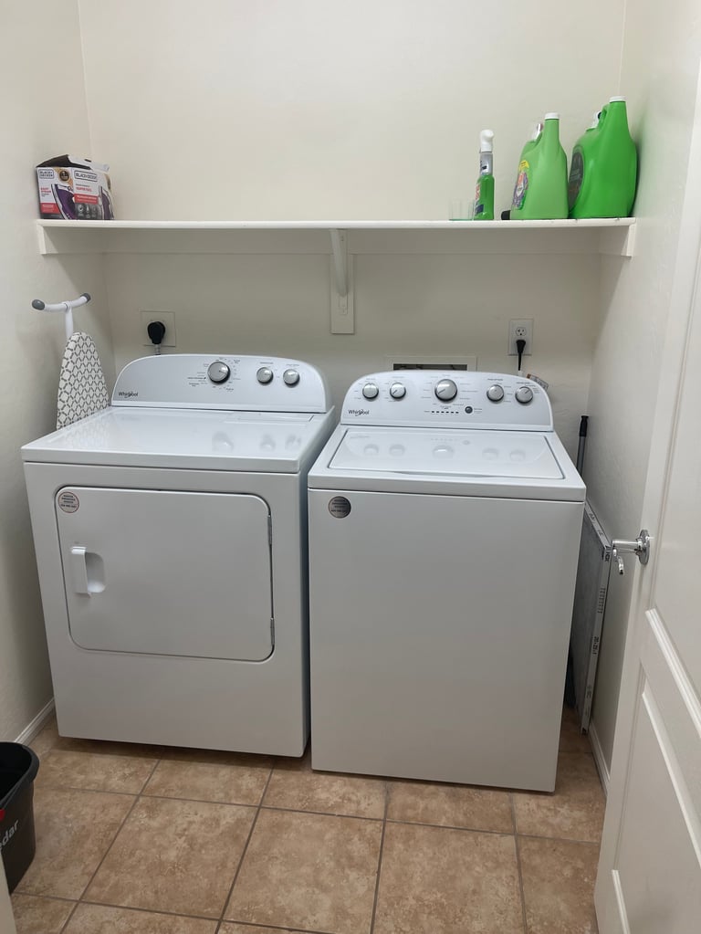 A laundry room with a white dryer on the left and washer on the right, with cleaning supplies on a shelf above